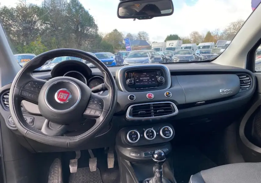 Intérieur de la Fiat 500X noir, vue du poste de conduite avec volant, tableau de bord et levier de vitesses manuelle visibles.