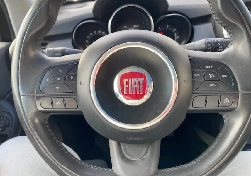 Vue rapprochée du volant noir de la Fiat 500X 2016 avec commandes intégrées et logo central rouge.