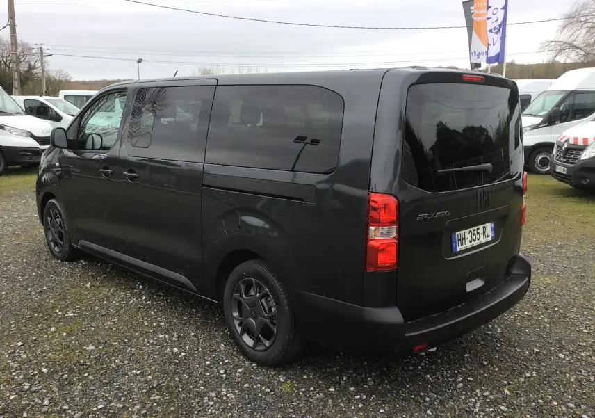 Vue 3/4 arrière droite d’un FIAT Scudo Combi gris titane avec vitres latérales surteintées et hayon fermé sur un parking extérieur.