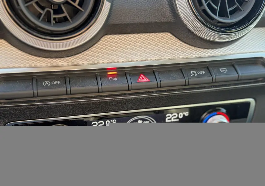 Gros plan sur la console centrale de l'Audi Q2 35 TFSI 2024, boutons de contrôle avec témoin lumineux rouge actif.