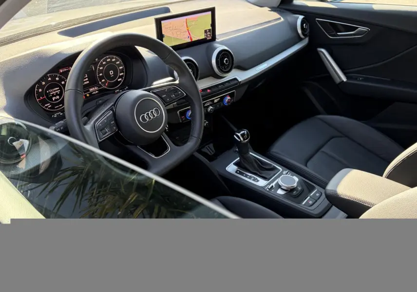 Vue intérieure côté conducteur de l'Audi Q2 35 TFSI S-Line 2024, volant cuir, écran GPS et tableau de bord numérique.
