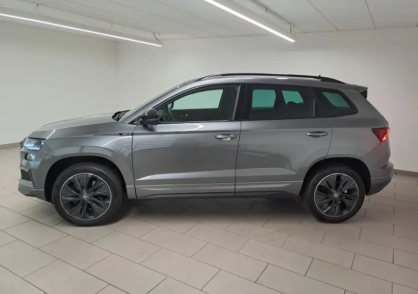 Vue latérale droite d'un Skoda Karoq gris graphite métallisé 2025 avec jantes noires et hayon électrique en intérieur.