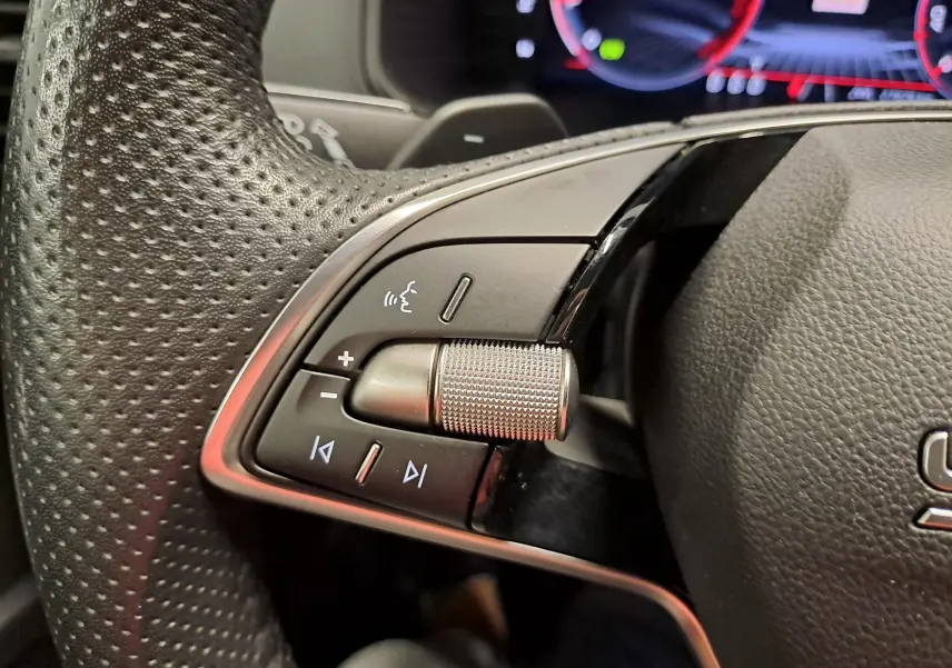 Gros plan sur les commandes gauche du volant perforé du Skoda Karoq 2025, avec molette et boutons multifonctions.