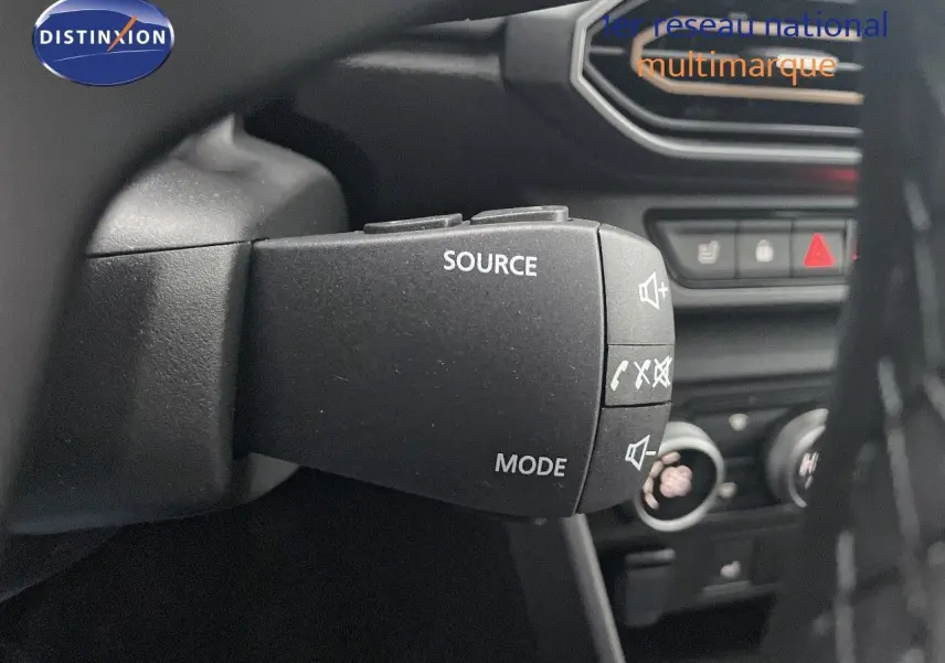 Gros plan sur la commande audio au volant du Dacia Jogger gris schiste, avec tableau de bord et commandes clim visibles en arrière-plan.