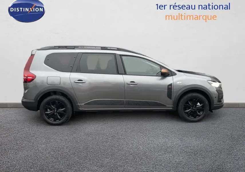 Vue latérale droite d'un Dacia Jogger gris schiste métallisé avec jantes noires et barres de toit, sur fond neutre.