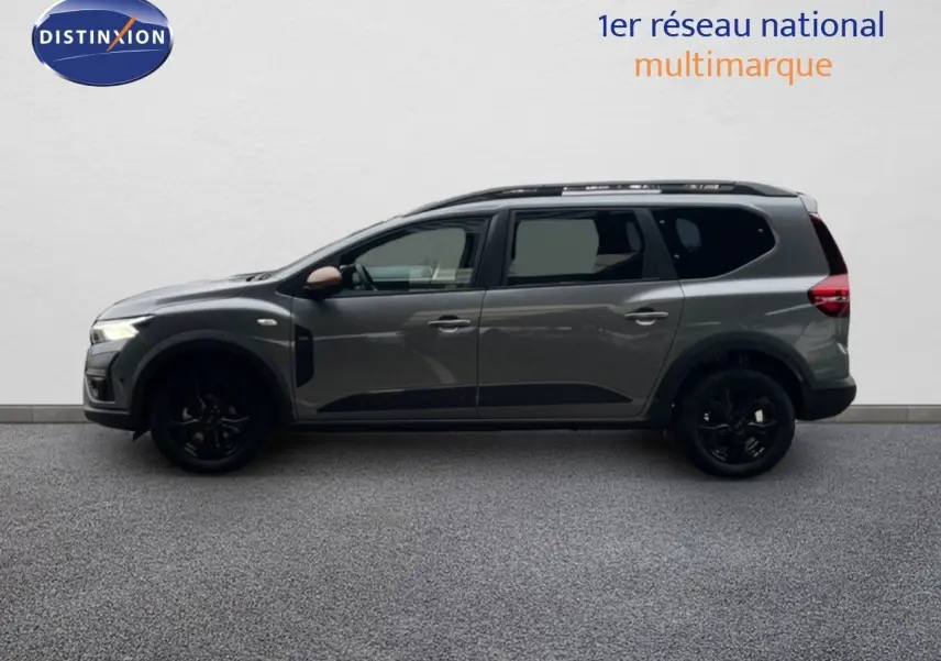 Profil latéral droit du Dacia Jogger gris schiste métal 7 places avec jantes noires et barres de toit visibles.