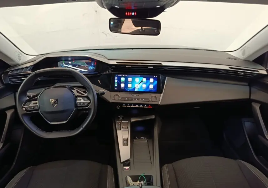 Vue intérieure avant de la Peugeot 308 2023, tableau de bord noir avec écran tactile central et volant cuir multifonctions.