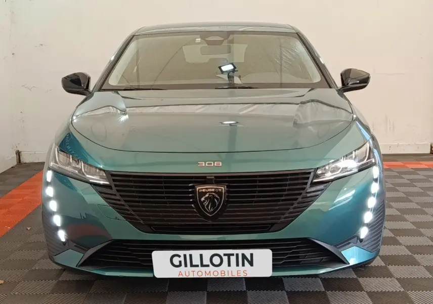 Vue frontale d'une Peugeot 308 2023 vert métallisé avec feux LED verticaux et calandre noire distinctive.
