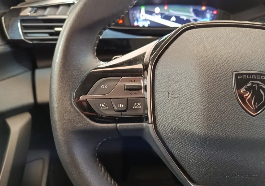 Gros plan sur le volant cuir noir de la Peugeot 308 2023 avec commandes multifonctions et logo lion central.