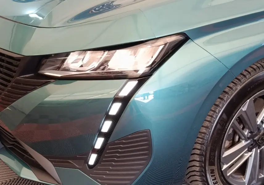 Gros plan sur l'avant droit bleu métallisé du Peugeot 308 2023, mettant en valeur les phares LED et la jante alliage.