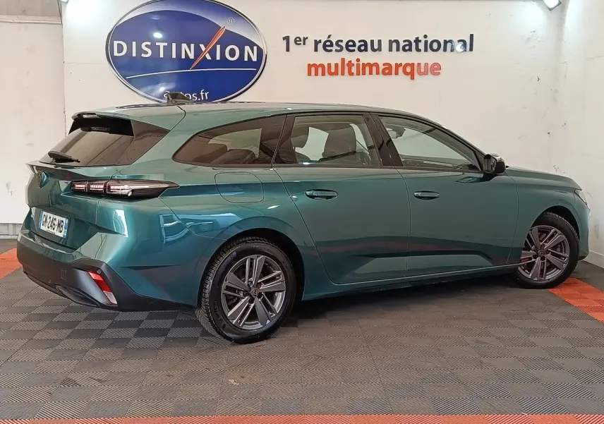 Peugeot 308 break 2023 vert métallisé vue 3/4 arrière côté droit en intérieur showroom.