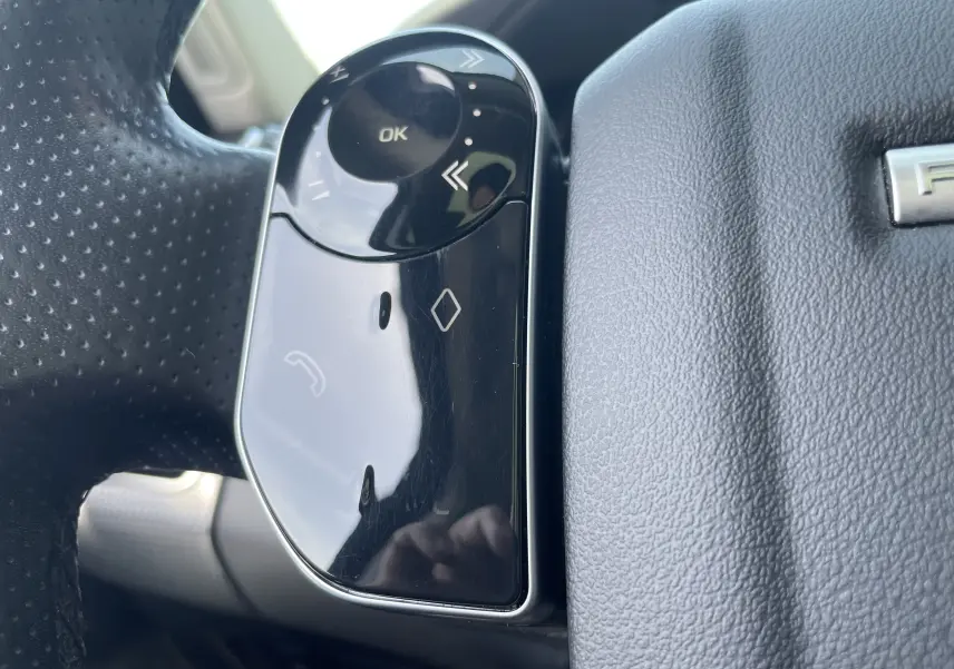 Gros plan sur les commandes gauche du volant en cuir noir du Range Rover Sport gris, avec boutons multifonctions brillants.