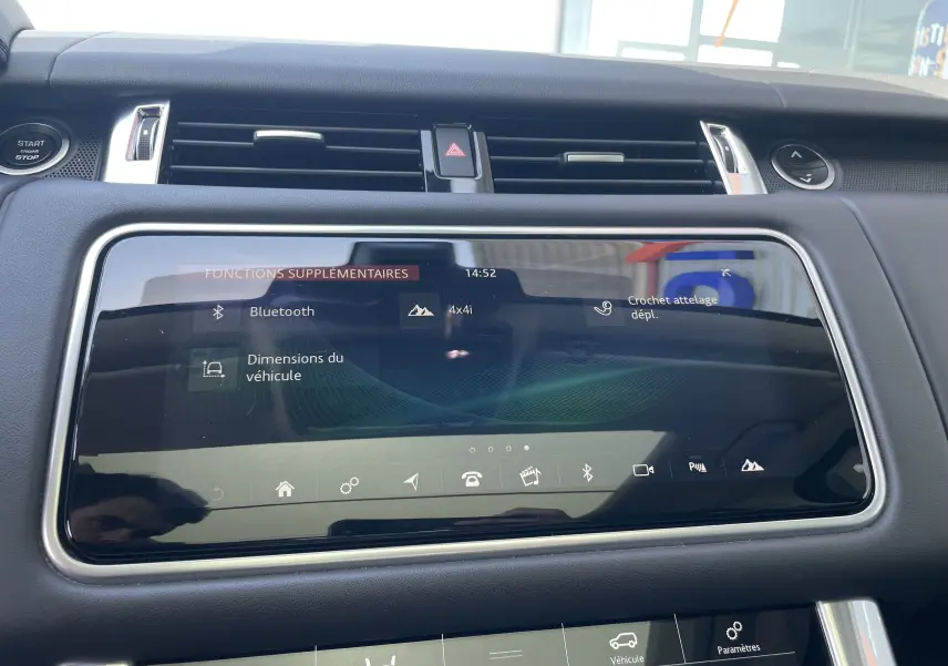 Écran tactile central du Range Rover Sport gris, affichant les fonctions Bluetooth et crochet d'attelage, vue intérieure frontale.