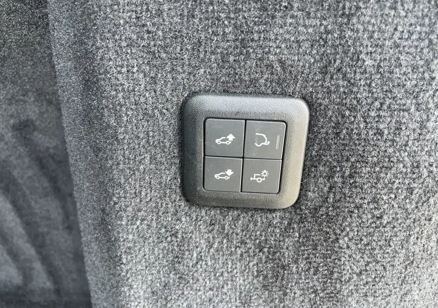 Gros plan sur les boutons de commande du hayon et de l'attelage, sur la moquette grise du coffre du Range Rover Sport gris Eiger.