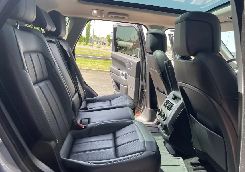 Vue intérieure côté gauche du Range Rover Sport gris Eiger, montrant les sièges arrière en cuir noir et le toit panoramique ouvert.