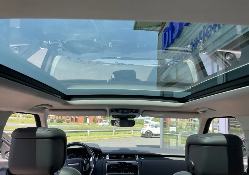 Vue intérieure du toit panoramique et tableau de bord du Range Rover Sport gris Eiger avec sellerie cuir noir.