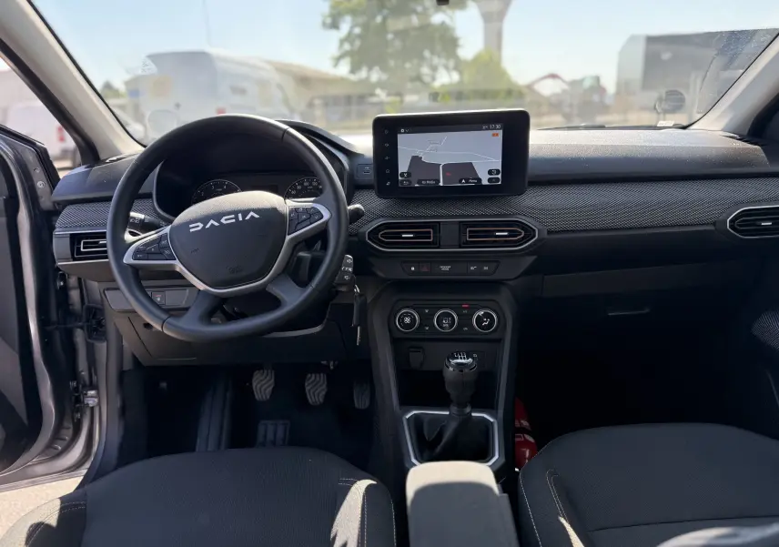 Vue intérieure avant du tableau de bord et volant de la Dacia Sandero Stepway 2025, avec écran tactile et levier de vitesse manuel.