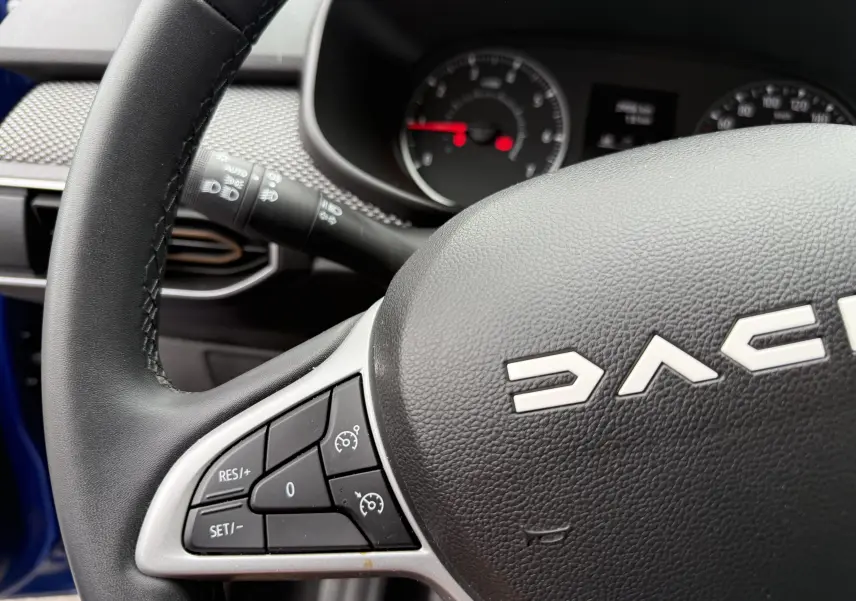 Gros plan sur le volant noir de la Dacia Sandero Stepway 2025, montrant les commandes de régulateur de vitesse côté gauche.