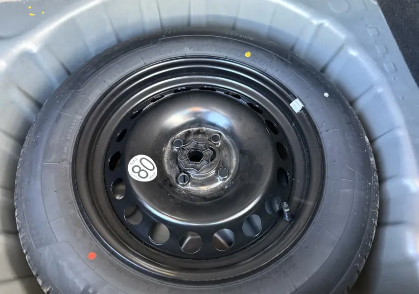 Gros plan sur la roue de secours noire montée sur jante acier, logée dans le coffre du Dacia Sandero Stepway gris schiste.