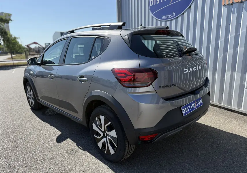 Vue 3/4 arrière droite d'une Dacia Sandero Stepway gris schiste métal avec barres de toit et jantes distinctives.