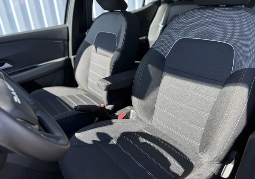 Gros plan sur les sièges avant en tissu gris et noir du Dacia Sandero Stepway 2025, avec accoudoir côté droit visible.