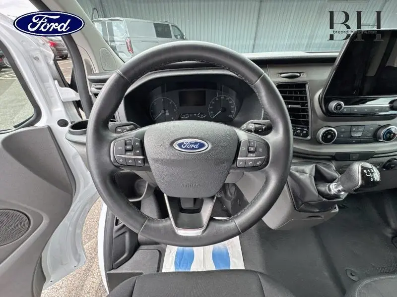 Vue intérieure centrée sur le volant cuir et levier de vitesse manuel du Ford Transit Custom blanc Glacier 2023.