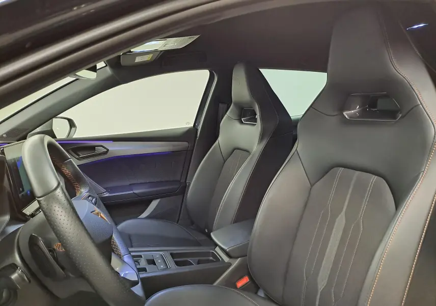 Intérieur avant droit de la CUPRA Leon 2023 gris magnétique, sièges sport noirs avec surpiqûres orange et volant cuir perforé.