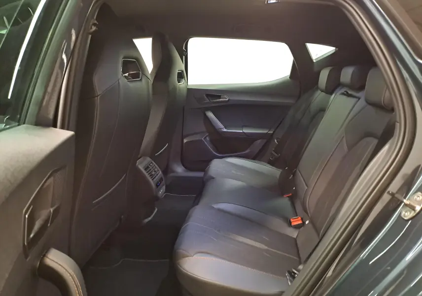 Vue intérieure arrière côté droit de la CUPRA Leon 1.5 eTSI 2023 gris magnétique avec sièges en cuir noir et surpiqûres orange.