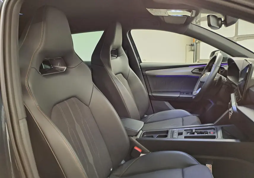 Intérieur de la CUPRA Leon 2023 vu côté gauche, sièges sport noirs avec surpiqûres orange et ambiance lumineuse violette.