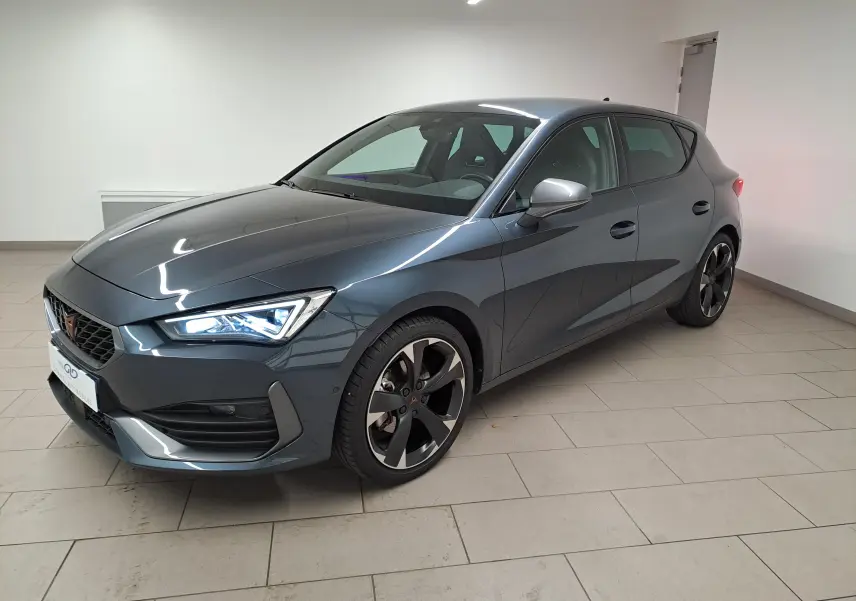Vue 3/4 avant droite d'une CUPRA Leon 1.5 eTSI 150 ch gris magnétique avec jantes noires distinctives en intérieur neutre.