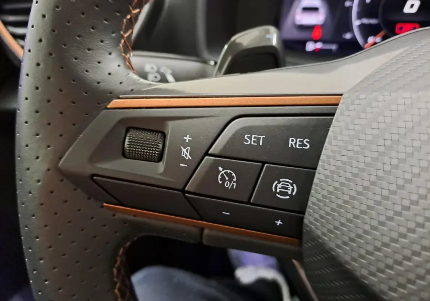 Gros plan sur les commandes de régulateur de vitesse au volant perforé avec surpiqûres cuivrées d'une CUPRA Leon 2023 gris magnétique.