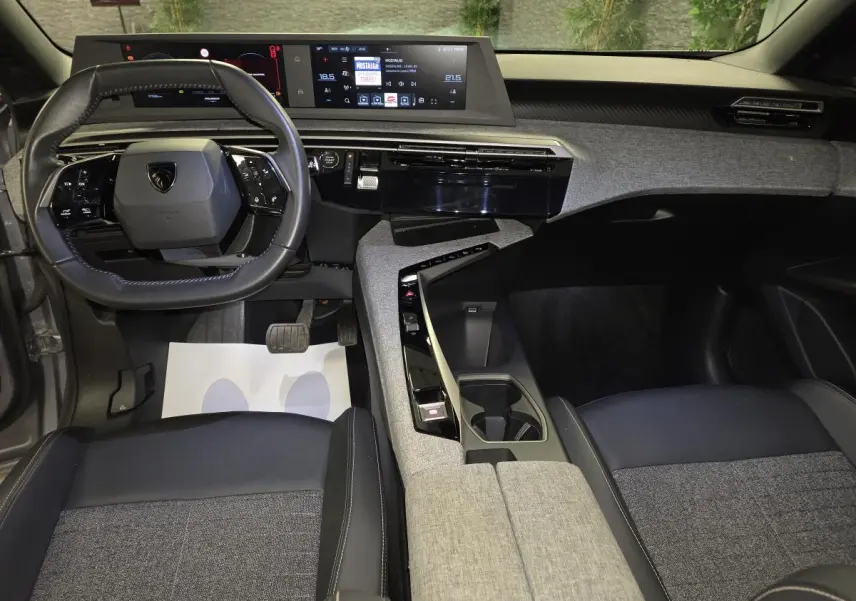 Vue intérieure avant du Peugeot 3008 Hybrid 2025, tableau de bord et console centrale avec décor tissu gris et noir laqué.
