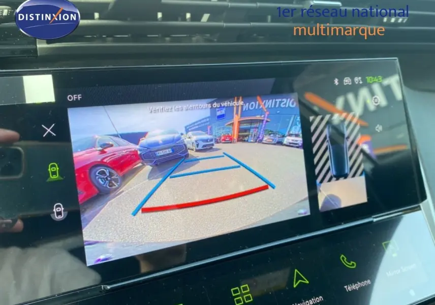 Écran de caméra de recul montrant une Peugeot 308 blanche vue de l'arrière avec des voitures garées à côté.