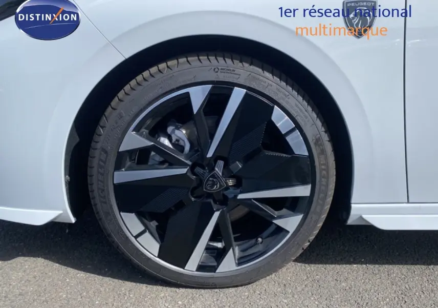 Gros plan sur la roue avant droite de la Peugeot 308 Hybrid 145ch GT blanche, avec jante noire et argentée au design moderne.