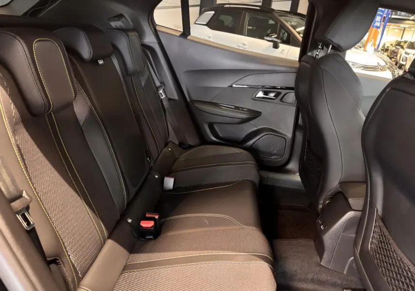 Vue intérieure arrière droite du Peugeot 2008 1.2i Hybrid GT 2025, sièges noirs avec surpiqûres vertes et panneaux de porte noirs.