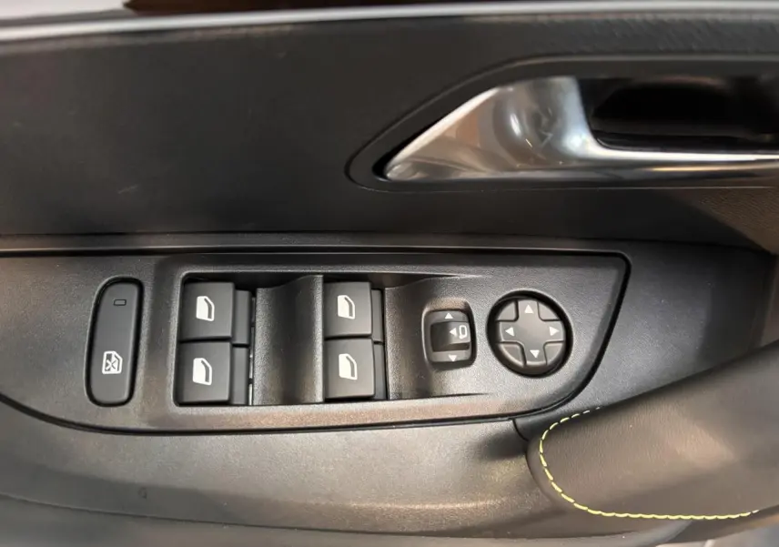 Gros plan sur les commandes de lève-vitres et rétroviseurs noirs avec surpiqûre vert Adamite sur porte avant gauche du Peugeot 2008 blanc.