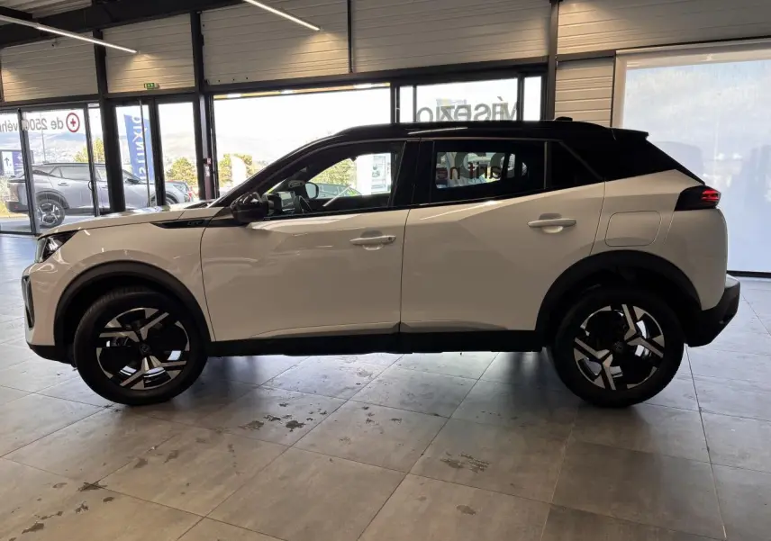 Vue de profil côté gauche d’un Peugeot 2008 blanc avec toit noir et jantes alliage bi-ton dans un showroom.