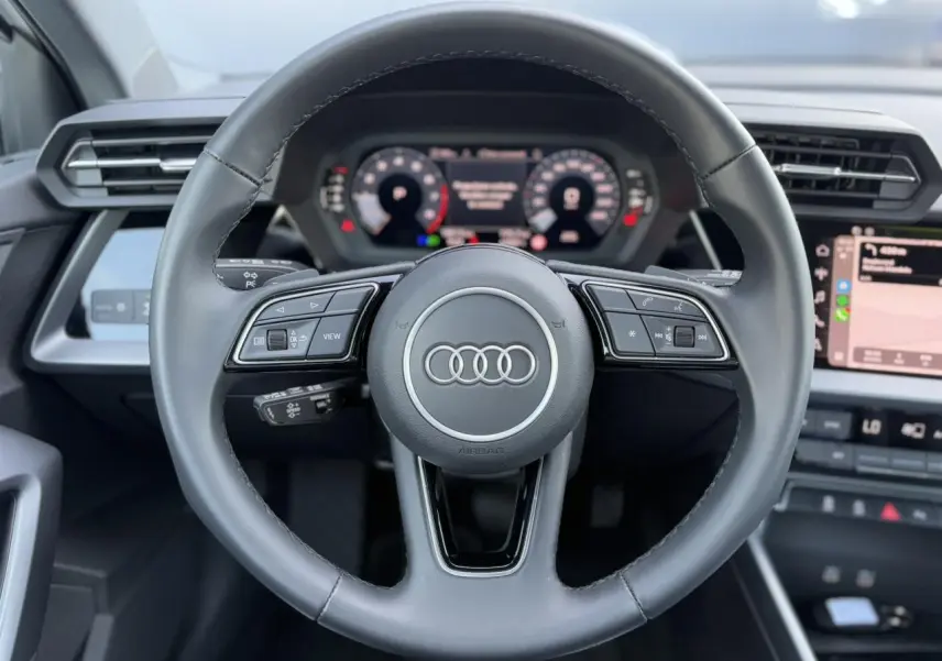Volant cuir noir multifonctions Audi A3 Sportback 2024 vu de face avec tableau de bord numérique et écran tactile.