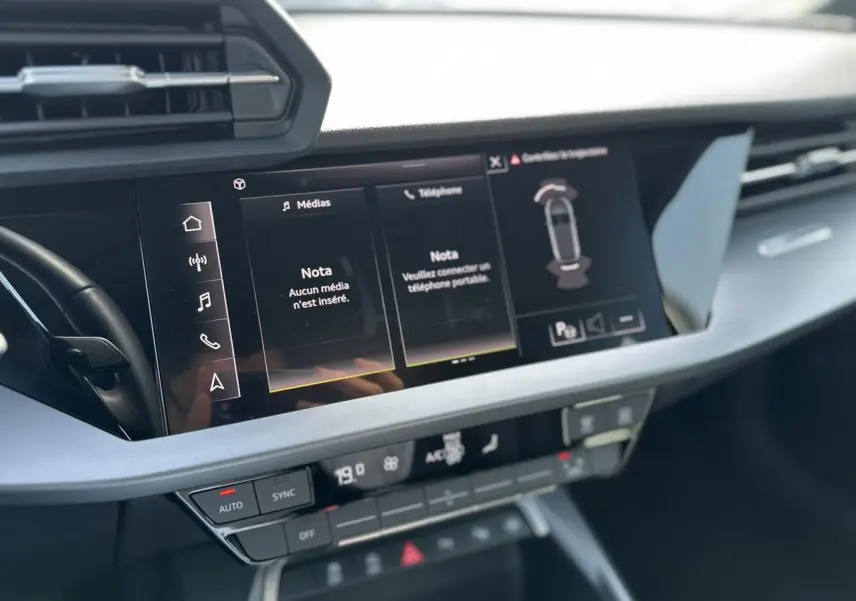 Vue rapprochée de la console centrale de l'Audi A3 Sportback 2024 blanche, avec écran tactile multimédia allumé.