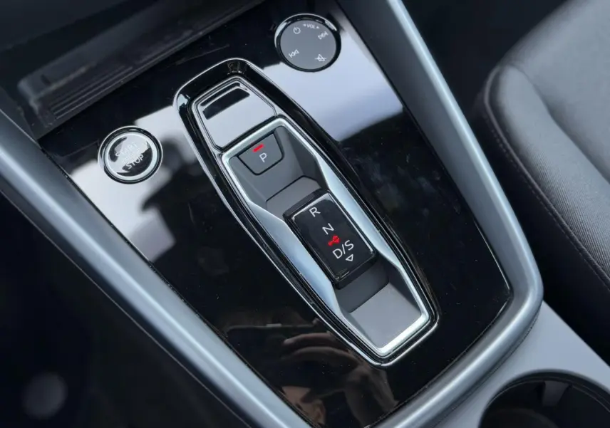 Vue rapprochée de la console centrale noire brillante avec levier de vitesses automatique et bouton start/stop de l'Audi A3 Sportback 2024.