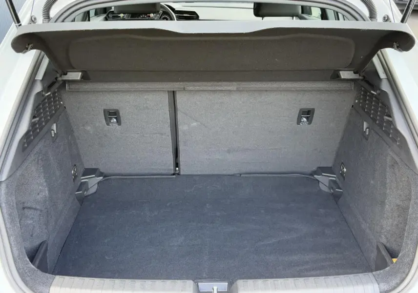 Coffre ouvert vu de l'arrière de l'Audi A3 Sportback blanc Arkona, espace de chargement vide et tapis gris.