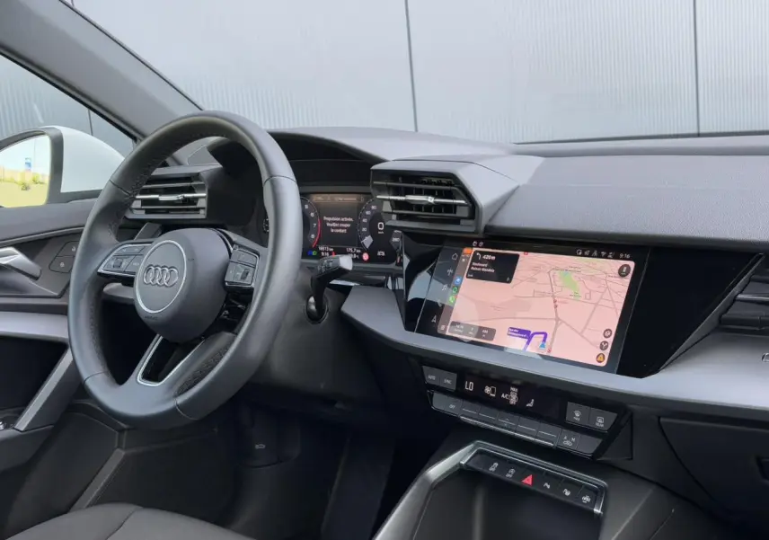 Vue intérieure côté conducteur de l'Audi A3 Sportback 2024, tableau de bord avec écran tactile de navigation allumé.
