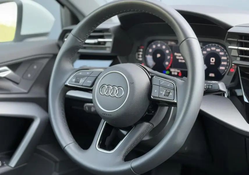 Vue rapprochée du volant cuir 3 branches multifonctions de l'Audi A3 Sportback 2024, intérieur noir moderne.