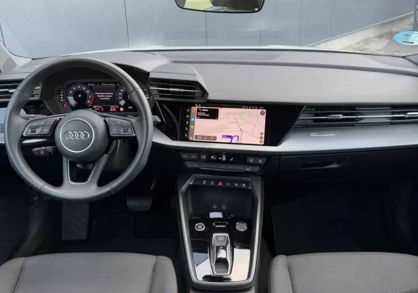 Vue intérieure avant de l'Audi A3 Sportback 2024, tableau de bord noir avec écran tactile et volant multifonctions cuir.