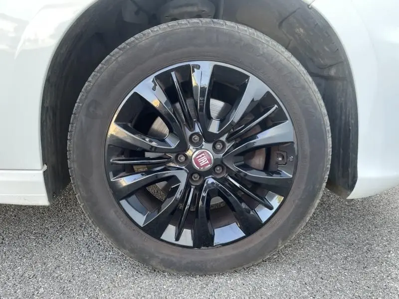 Gros plan sur la roue avant gauche d'une Fiat Tipo blanche de 2019 avec jante noire brillante et logo Fiat central.