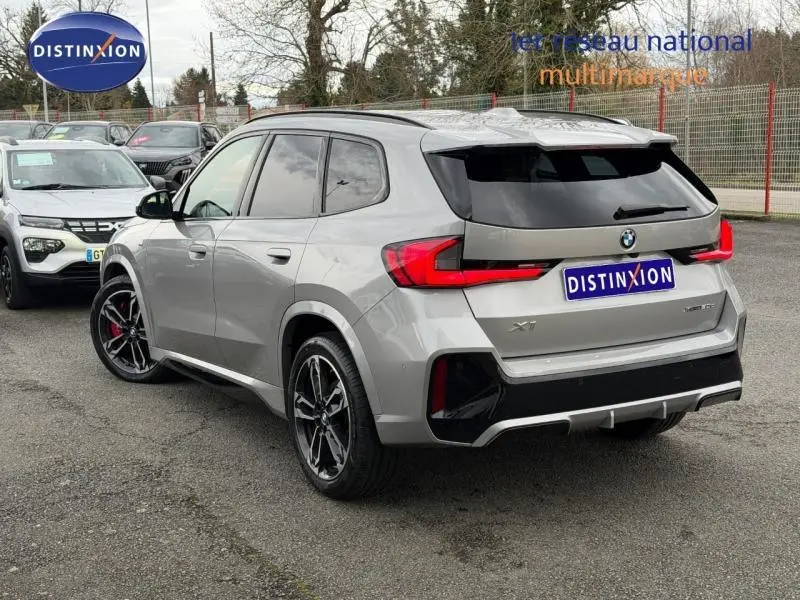 BMW X1 xDrive20d 2025 gris Spacesilber métal, vue 3/4 arrière droit avec jantes noires et feux LED rouges.