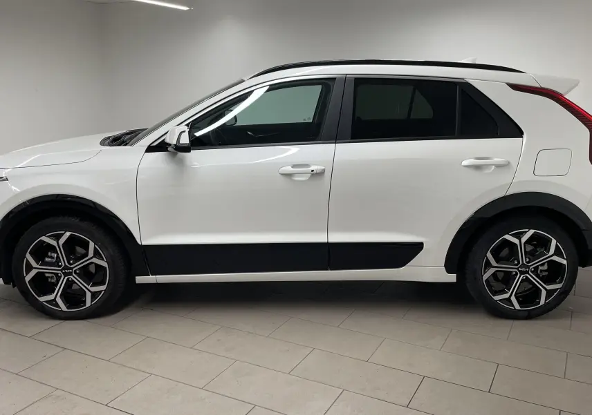 Vue de profil côté gauche du KIA NIRO 2025 blanc hybride avec jantes alliage noires et détails noirs contrastants.