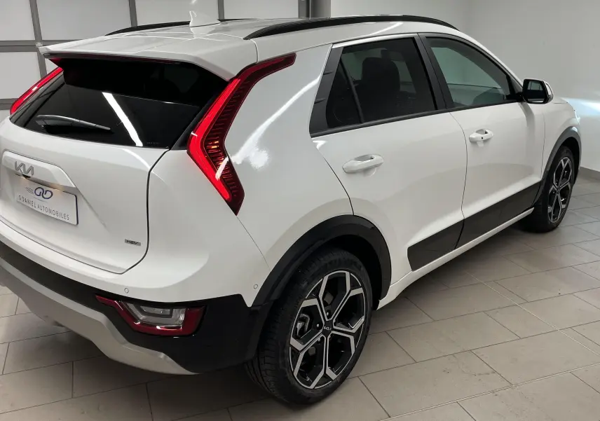 Vue 3/4 arrière droite du Kia Niro blanc 2025 hybride avec feux arrière en forme de boomerang et jantes noires.