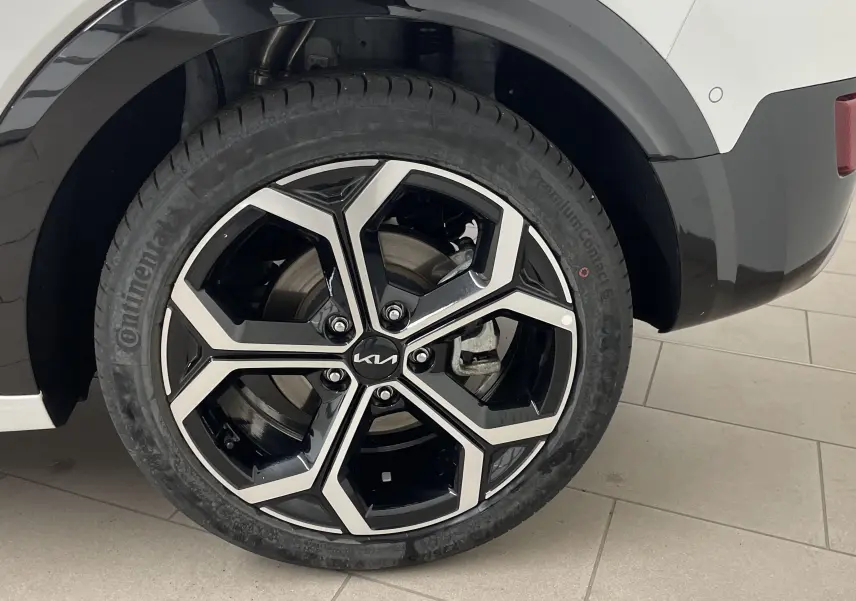 Gros plan sur la roue arrière droite blanche du KIA NIRO 2025 avec jante noire et argent au design géométrique.