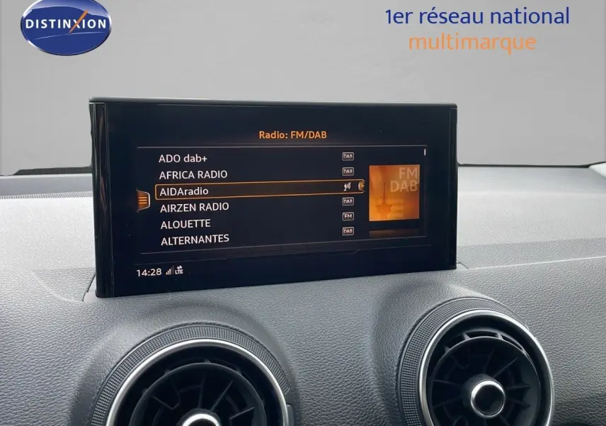 Écran central du tableau de bord d'un Audi Q2 2023 noir, affichant les stations radio FM/DAB.